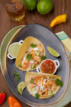 Two shrimp tacos with salsa guacamole beer garnished with mini bell pepper and lime.の写真素材
