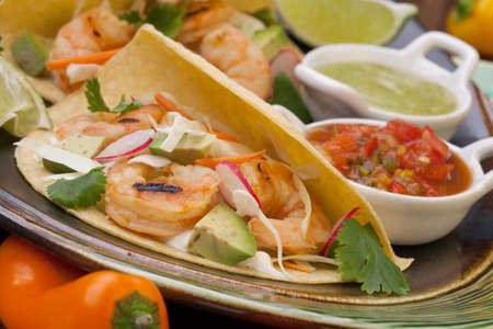 Two shrimp tacos with salsa guacamole beer garnished with mini bell pepper and lime.の写真素材