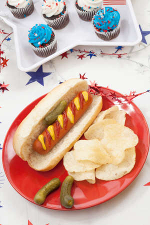 Hot dog chips and pickled cucumbers. Angel food fruit cakes and muffins on 4th of July in patriotic theme in background.の写真素材