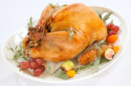 Roasted turkey on tray garnished with red grapes figs kumquat and herbs over white backgroundの写真素材