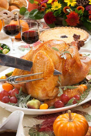 Carving roasted turkey on a server tray garnished with fresh figs grape kumquat and herbs on fall harvest table. Red wine side dishes pie and gravy. Decoraded with mini pumpkins candels and flowers.の写真素材