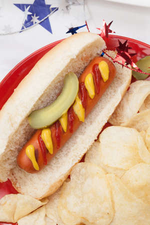 Hot dog chips and pickled cucumbers. Angel food fruit cakes and muffins on 4th of July in patriotic theme in background.の写真素材