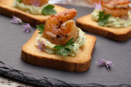 Closeup of grilled shrimp canape with spicy guacamole and parsley. Couple of tropical cocktail drinks in background.の写真素材