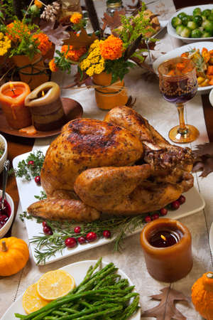 Roasted turkey garnished with cranberries on a rustic style table decoraded with pumpkins, gourds, asparagus, brussel sprouts, baked vegetables, pie, flowers, and candles.の写真素材