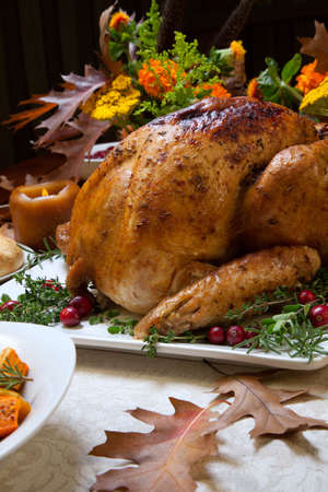 Roasted turkey garnished with cranberries on a rustic style table decoraded with pumpkins, gourds, asparagus, brussel sprouts, baked vegetables, pie, flowers, and candles.の写真素材