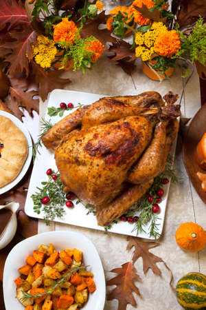 Roasted turkey garnished with cranberries on a rustic style table decoraded with pumpkins, gourds, asparagus, brussel sprouts, baked vegetables, pie, flowers, and candles.の写真素材