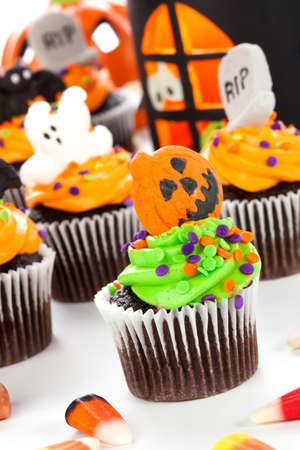Halloween cupcake with jack-o'-lantern and bat decorations surrounded by Halloween cupcakes, corn candies, and decoration.の写真素材