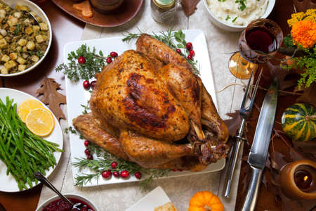 Roasted turkey garnished with cranberries on a rustic style table decoraded with pumpkins, gourds, asparagus, brussel sprouts, baked vegetables, pie, flowers, and candles.の写真素材