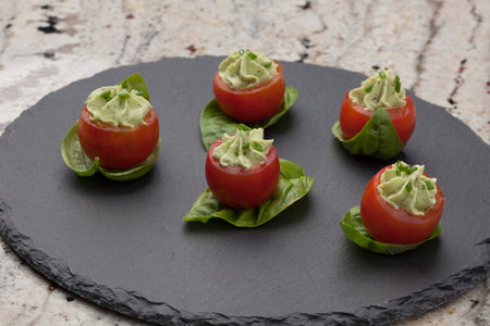 Closeup of avocado cream cheese stuffed campari tomatoes on basil leaves. Couple of tropical...
