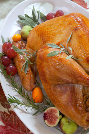 Roasted turkey on a server tray garnished with fresh figs, grape, kumquat, and herbs on fall harvest table. Red wine, side dishes, pie, and gravy. Decoraded with mini pumpkins, candels, and flowers.の写真素材