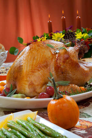 Roasted turkey on a server tray garnished with fresh figs, grape, kumquat, and herbs on fall harvest table. Red wine, side dishes, pie, and gravy. Decoraded with mini pumpkins, candels, and flowers.の写真素材