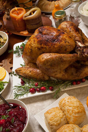 Roasted turkey garnished with cranberries on a rustic style table decoraded with pumpkins, gourds, asparagus, brussel sprouts, baked vegetables, pie, flowers, and candles.の写真素材