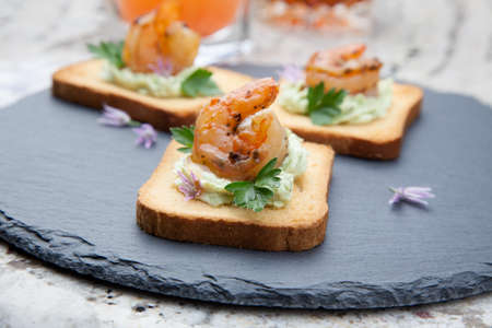 Closeup of grilled shrimp canape with spicy guacamole and parsley. Couple of tropical cocktail drinks in background.の写真素材