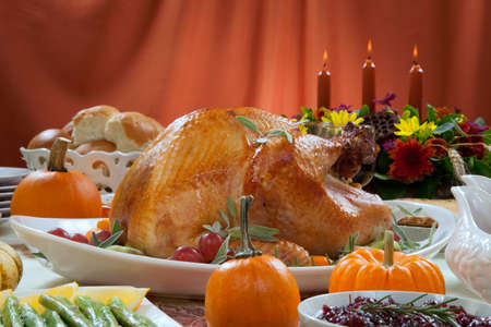 Roasted turkey on a server tray garnished with fresh figs, grape, kumquat, and herbs on fall harvest table. Red wine, side dishes, pie, and gravy. Decoraded with mini pumpkins, candels, and flowers.の写真素材