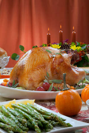 Roasted turkey on a server tray garnished with fresh figs, grape, kumquat, and herbs on fall harvest table. Red wine, side dishes, pie, and gravy. Decoraded with mini pumpkins, candels, and flowers.の写真素材