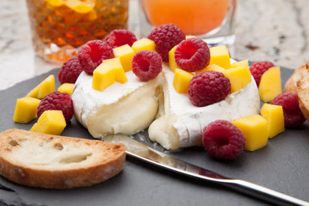 Warm baked Brie cheese with fresh mango and raspberries - great snack for cocktail party. Couple of cocktails in background.の写真素材