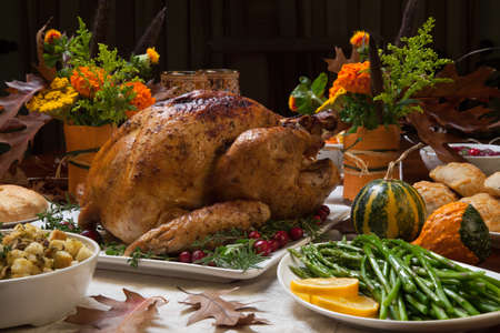 Roasted turkey garnished with cranberries on a rustic style table decoraded with pumpkins, gourds, asparagus, brussel sprouts, baked vegetables, pie, flowers, and candles.の写真素材
