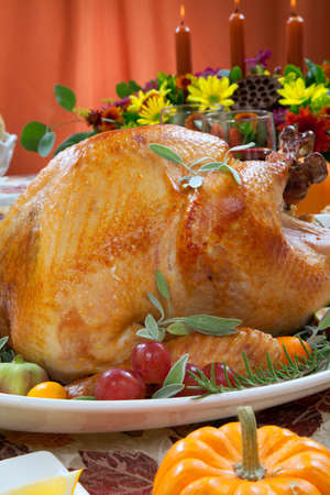 Roasted turkey on a server tray garnished with fresh figs, grape, kumquat, and herbs on fall harvest table. Red wine, side dishes, pie, and gravy. Decoraded with mini pumpkins, candels, and flowers.の写真素材