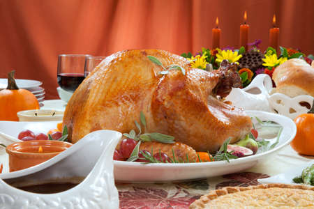 Roasted turkey on a server tray garnished with fresh figs, grape, kumquat, and herbs on fall harvest table. Red wine, side dishes, pie, and gravy. Decoraded with mini pumpkins, candels, and flowers.の写真素材