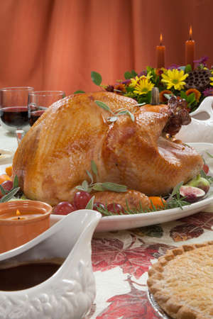 Roasted turkey on a server tray garnished with fresh figs, grape, kumquat, and herbs on fall harvest table. Red wine, side dishes, pie, and gravy. Decoraded with mini pumpkins, candels, and flowers.の写真素材