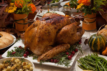 Roasted turkey garnished with cranberries on a rustic style table decoraded with pumpkins, gourds, asparagus, brussel sprouts, baked vegetables, pie, flowers, and candles.の写真素材