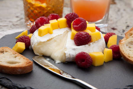 Warm baked Brie cheese with fresh mango and raspberries - great snack for cocktail party. Couple of cocktails in background.の写真素材