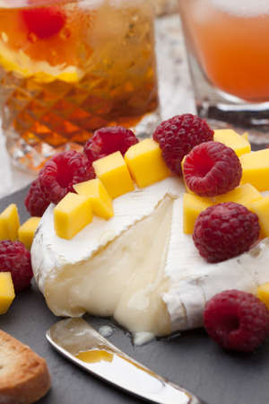 Warm baked Brie cheese with fresh mango and raspberries - great snack for cocktail party. Couple of cocktails in background.の写真素材