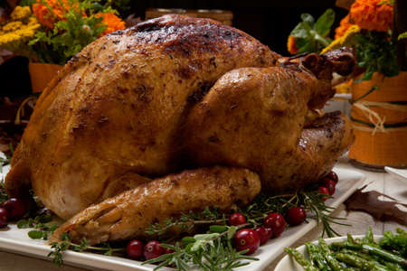Roasted turkey garnished with cranberries on a rustic style table decoraded with pumpkins, gourds, asparagus, brussel sprouts, baked vegetables, pie, flowers, and candles.の写真素材