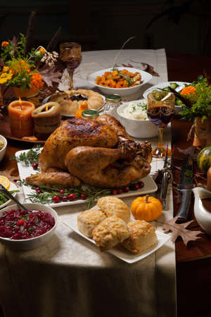 Roasted turkey garnished with cranberries on a rustic style table decoraded with pumpkins, gourds, asparagus, brussel sprouts, baked vegetables, pie, flowers, and candles.の写真素材