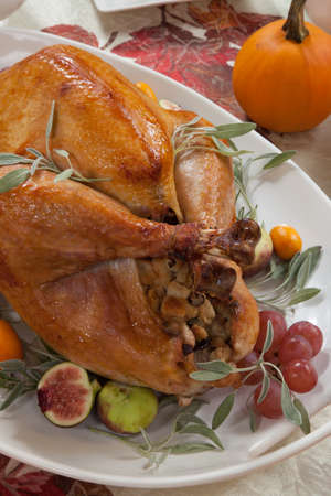 Roasted turkey on a server tray garnished with fresh figs, grape, kumquat, and herbs on fall harvest table. Red wine, side dishes, pie, and gravy. Decoraded with mini pumpkins, candels, and flowers.の写真素材
