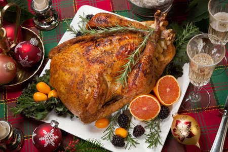 Roasted turkey with fresh fruits, flutes of champagne, Christmas tree, candles, and decorationsの写真素材