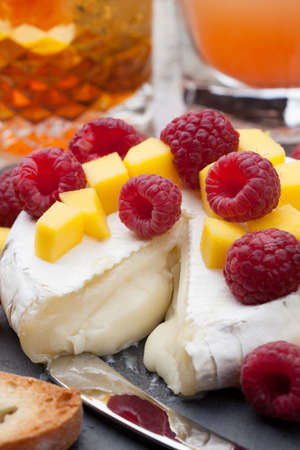 Warm baked Brie cheese with fresh mango and raspberries - great snack for cocktail party. Couple of cocktails in background.の写真素材