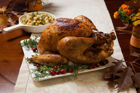 Roasted turkey garnished with cranberries on a rustic style table decoraded with pumpkins, gourds, asparagus, brussel sprouts, baked vegetables, pie, flowers, and candles.の写真素材