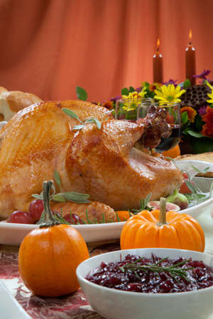 Roasted turkey on a server tray garnished with fresh figs, grape, kumquat, and herbs on fall harvest table. Red wine, side dishes, pie, and gravy. Decoraded with mini pumpkins, candels, and flowers.の写真素材