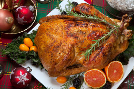 Roasted turkey with fresh fruits, flutes of champagne, Christmas tree, candles, and decorationsの写真素材