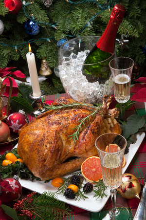 Roasted turkey with fresh fruits, flutes of champagne, Christmas tree, candles, and decorationsの写真素材