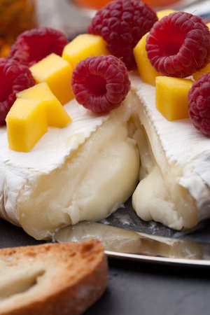 Warm baked Brie cheese with fresh mango and raspberries - great snack for cocktail party. Couple of cocktails in background.の写真素材