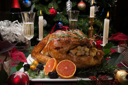 Roasted turkey with fresh fruits, flutes of champagne, Christmas tree, candles, and decorationsの写真素材