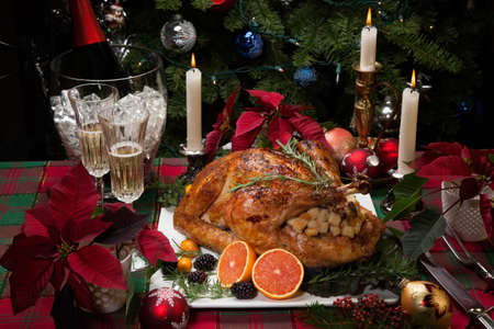 Roasted turkey with fresh fruits, flutes of champagne, Christmas tree, candles, and decorationsの写真素材