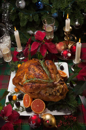 Roasted turkey with fresh fruits, flutes of champagne, Christmas tree, candles, and decorationsの写真素材