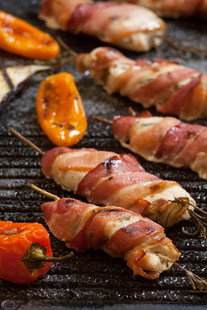 Grilled bacon-wrapped chicken tenders with lemon and rosemary on the grill wih grilled vegetables - peppers, and and eggplant.の写真素材