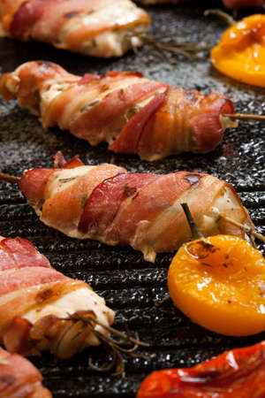 Grilled bacon-wrapped chicken tenders with lemon and rosemary on the grill wih grilled vegetables - peppers, and and eggplant.の写真素材