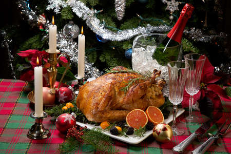 Roasted turkey with fresh fruits, flutes of champagne, Christmas tree, candles, and decorationsの写真素材