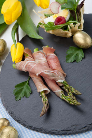Grilled asparagus wrapped in prosciutto and parmesan baskets filled with fresh garden salad. Easter decorated eggs, tulips flowers, holiday theme.の写真素材
