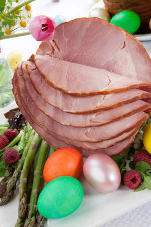 Whole baked honey sliced ham with fresh raspberry, asparagus, dyed Ester eggs, Easter cake, and cross buns. Spring flowers.の写真素材