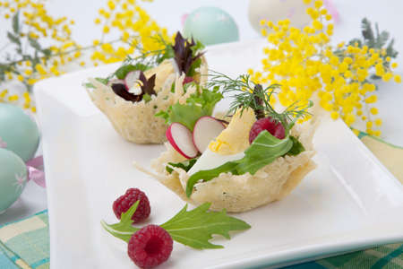 Parmesan baskets filled with fresh garden salad, hard-boiled eggs, and fresh raspberries. Easter decorated eggs, spring flowers, holiday theme. Over white.の写真素材