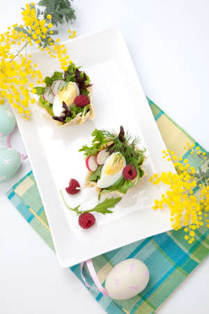 Parmesan baskets filled with fresh garden salad, hard-boiled eggs, and fresh raspberries. Easter decorated eggs, spring flowers, holiday theme. Over white.の写真素材
