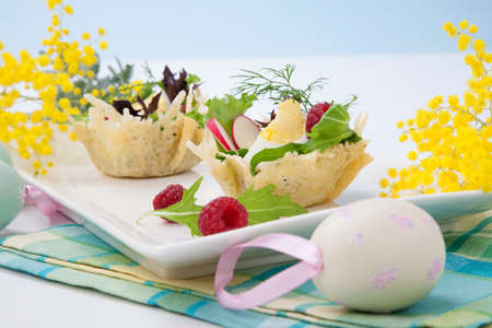 Parmesan baskets filled with fresh garden salad, hard-boiled eggs, and fresh raspberries. Easter decorated eggs, spring flowers, holiday theme. Over white.の写真素材
