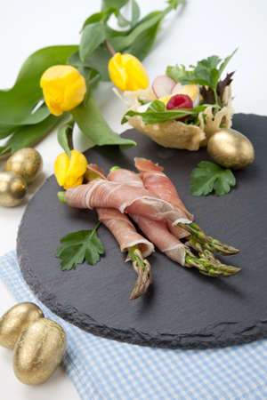 Grilled asparagus wrapped in prosciutto and parmesan baskets filled with fresh garden salad. Easter decorated eggs, tulips flowers, holiday theme.の写真素材
