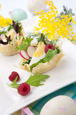 Parmesan baskets filled with fresh garden salad, hard-boiled eggs, and fresh raspberries. Easter decorated eggs, spring flowers, holiday theme. Over white.の写真素材